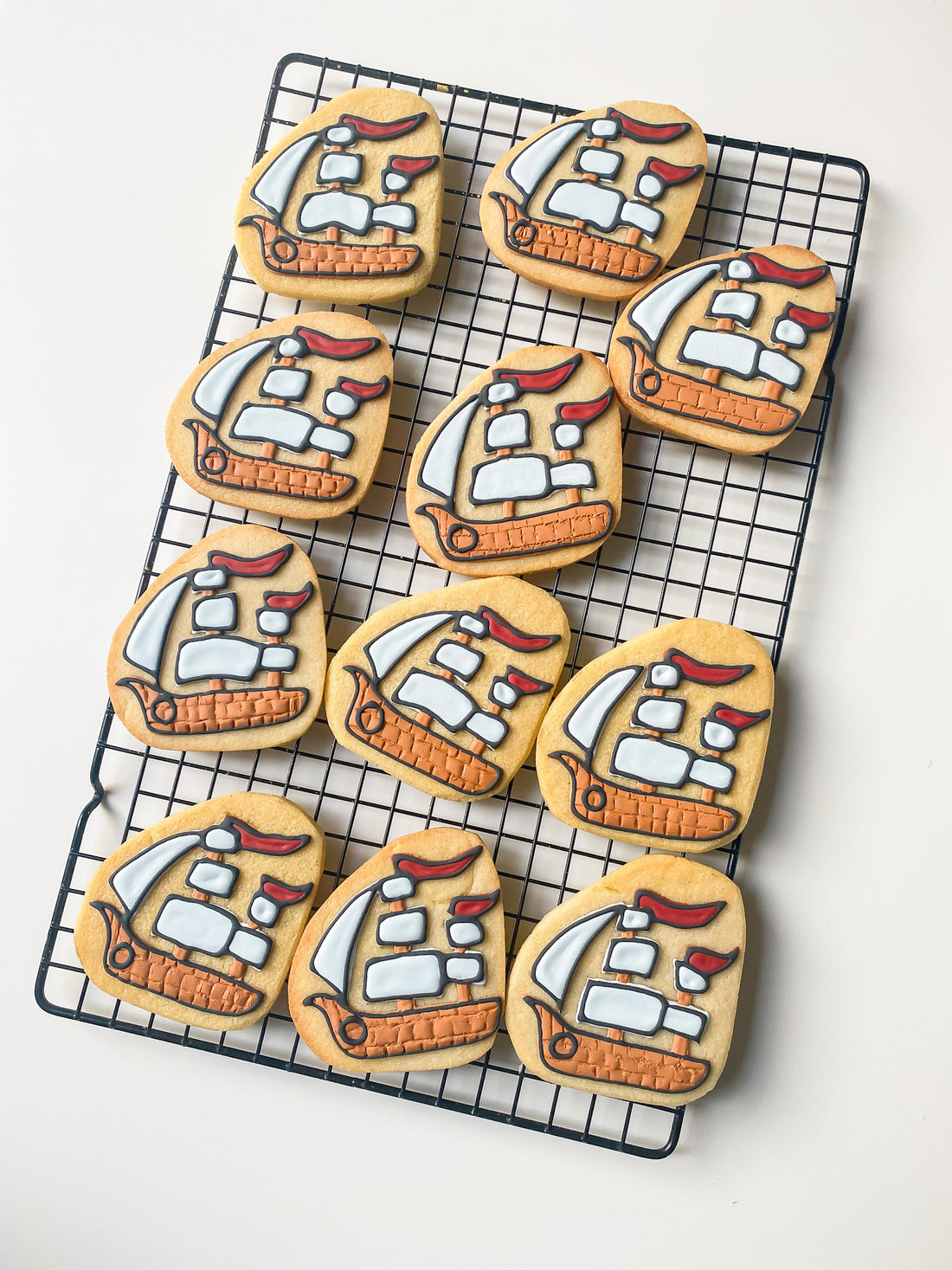 Hand-decorated pirate ship cookies arranged on a cooling rack by Reet Petite Bakery Co